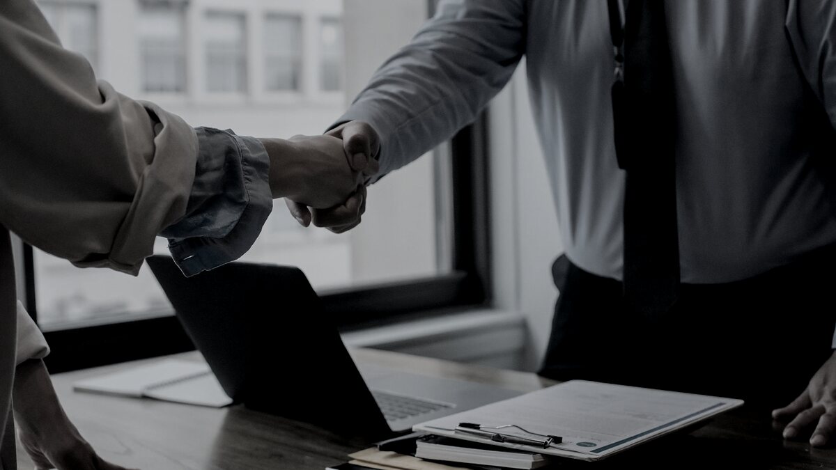 Sales representative shaking hands with a client partner over a laptop in a Rochester office