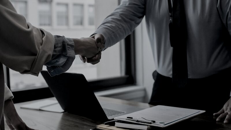 Sales representative shaking hands with a client partner over a laptop in a Rochester office