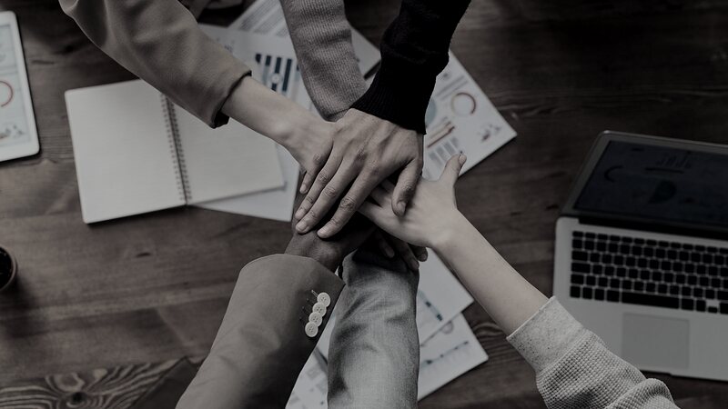 Team members joining hands over performance reports on a table